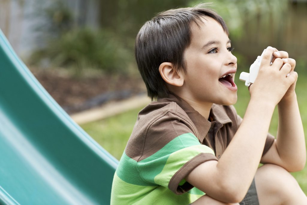 Boy using asthma inhaler in the garden